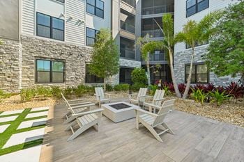 A patio with a table and chairs is surrounded by a garden and a building.